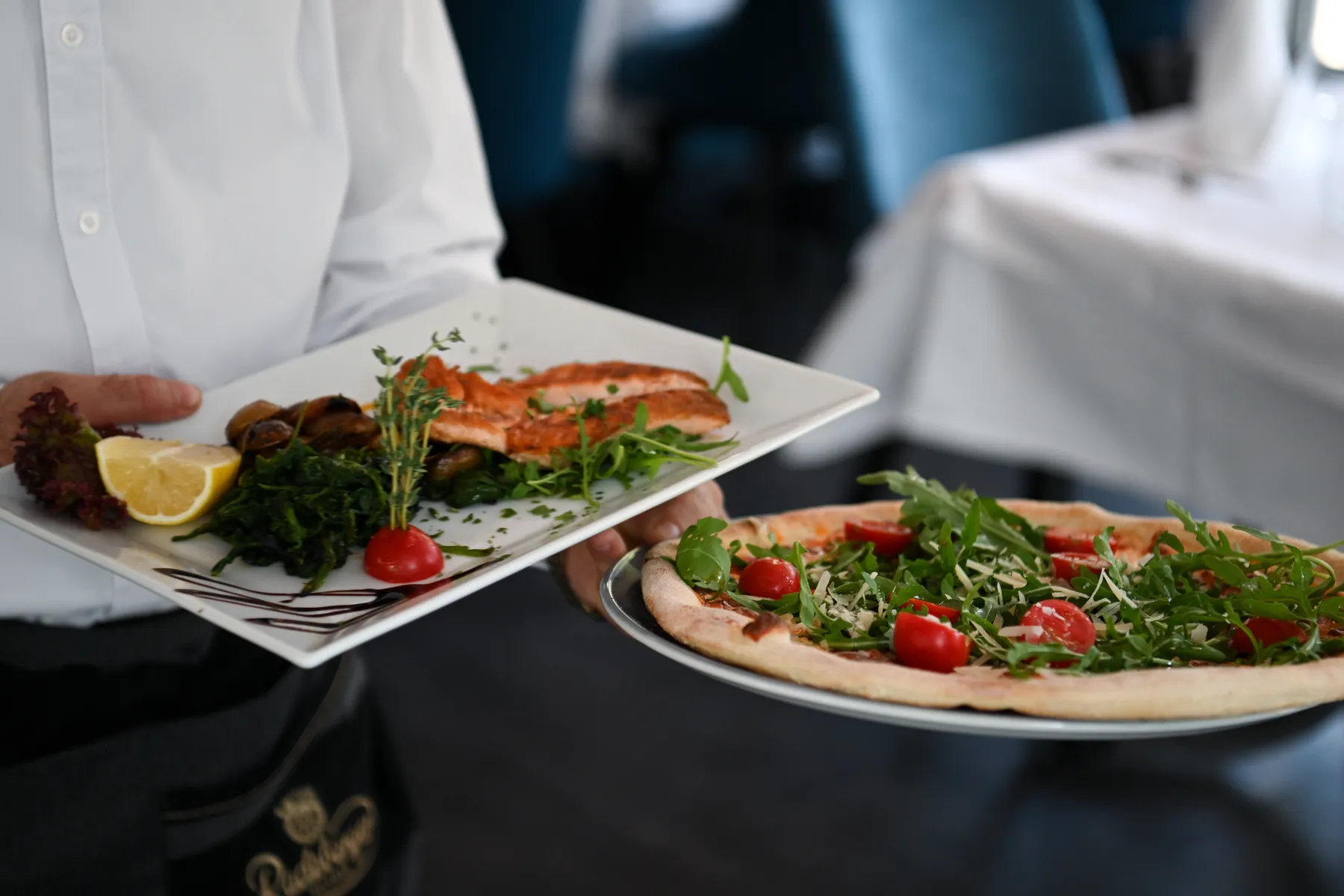 Teller aus der Küche: Pizza mit Rucola und Tomaten, dazu ein Fischteller und Rotwein